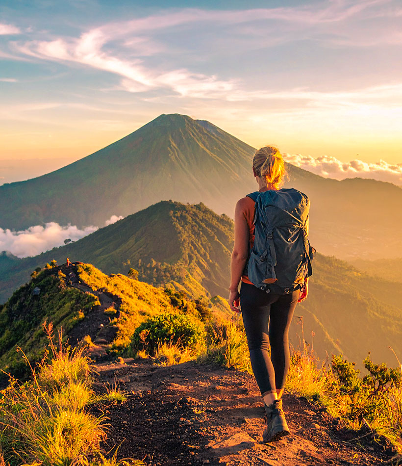 Frau blickt in der Abendstimmung auf einen Vulkan in Bali.